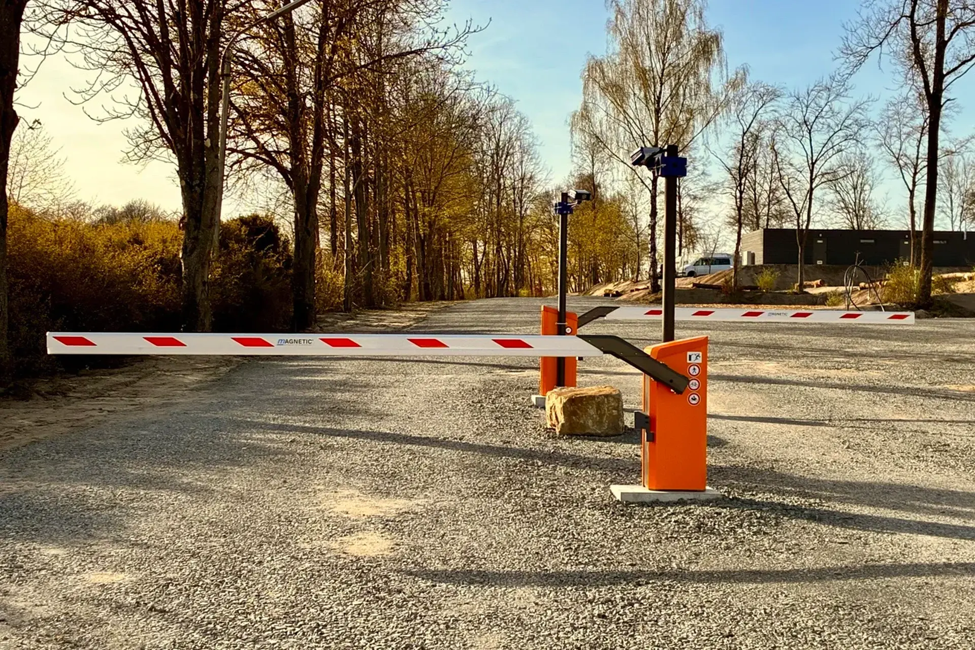 Einfahrt mit zwei Schrankenanlagen auf frischem Schotter, dahinter das Sanitärgebäude